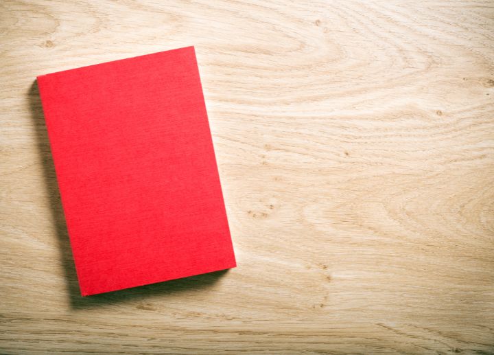 Red hardcover book placed on a light wooden surface